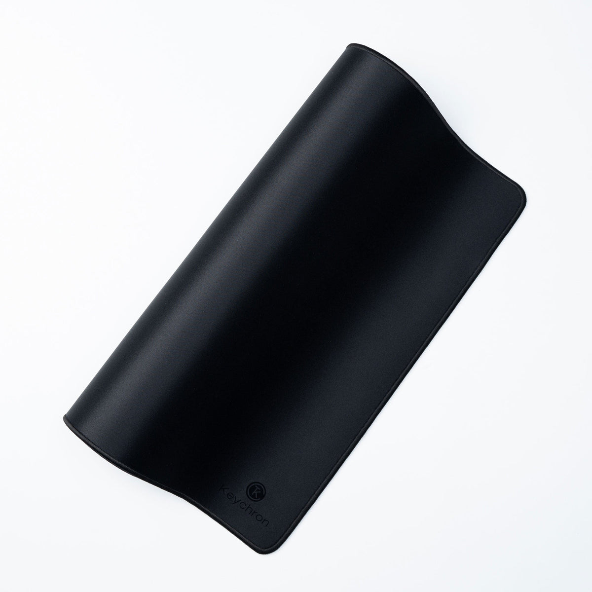 Keychron Desk Mat in Black, curled to show its flexibility and stitched edge